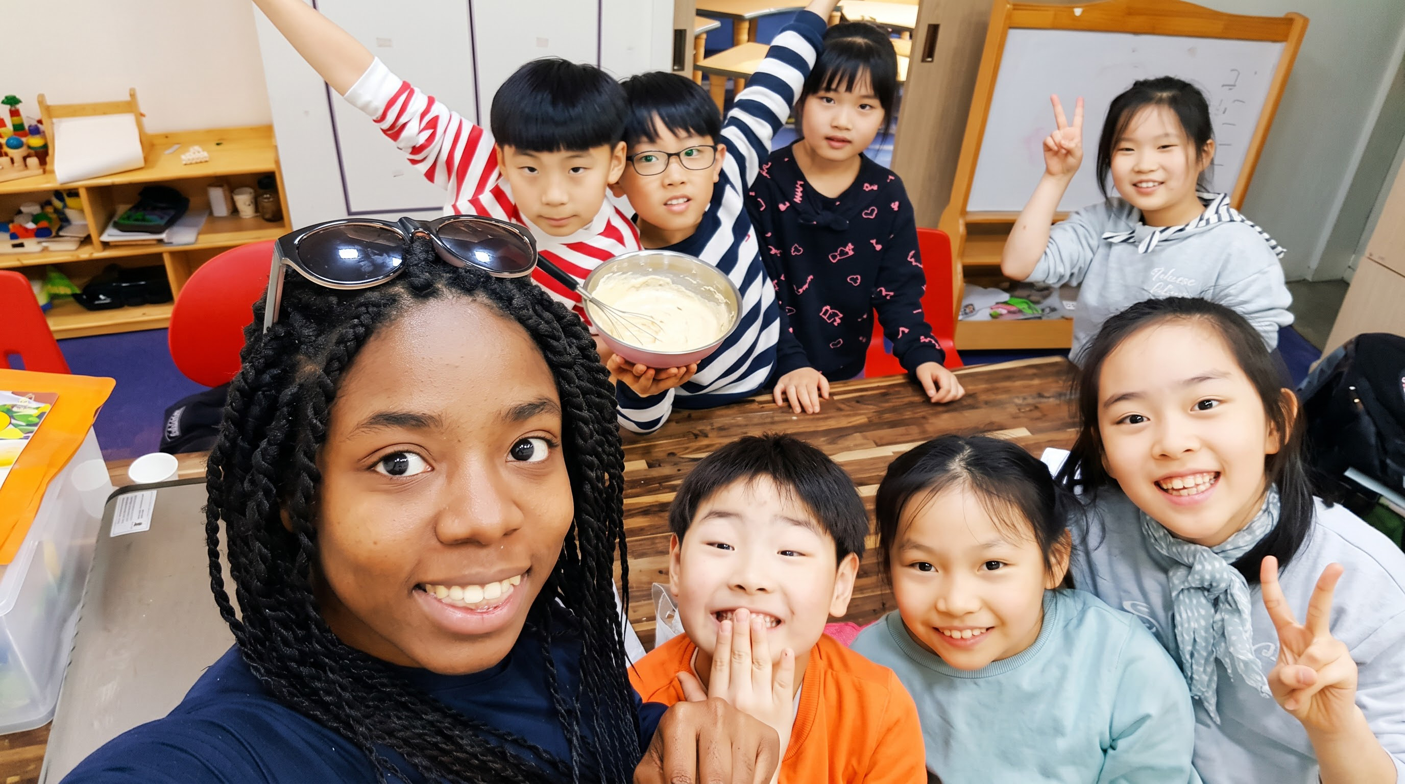 교실에서 선생님과 일곱 명의 아이들이 함께 웃으며 찍은 단체 사진